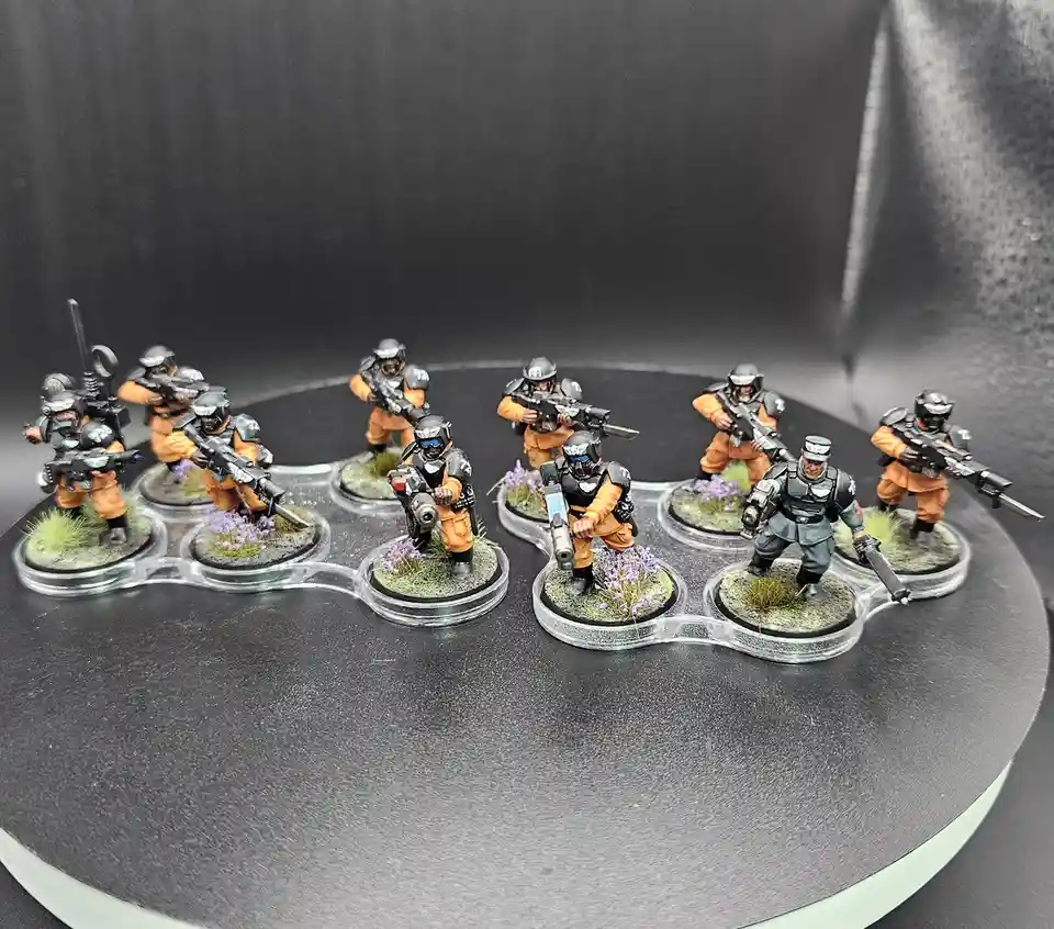 A photo shows nine painted miniature soldiers in orange and black armor, armed with futuristic weapons, arranged in a…