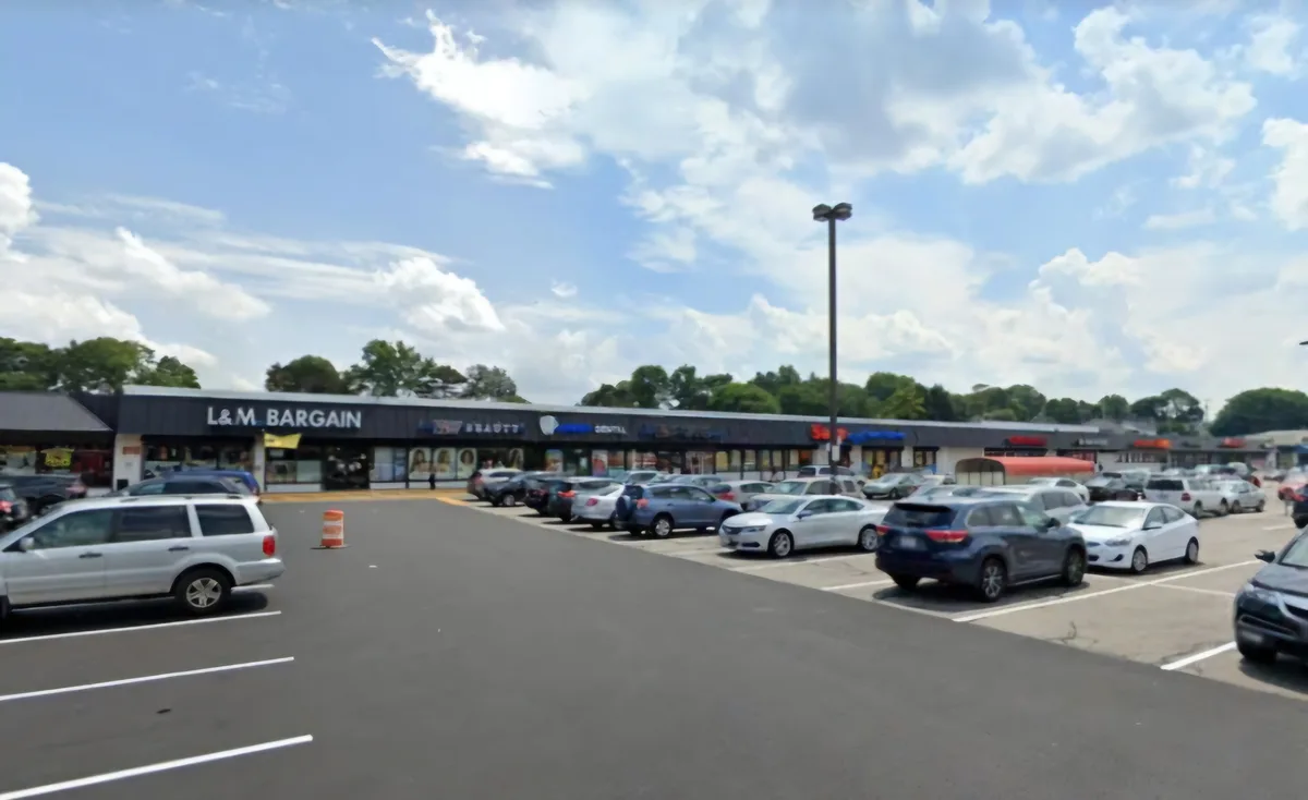An outdoor photo of a strip mall with a prominent sign reading 'L&M BARGAIN' above storefronts, surrounded by a large…