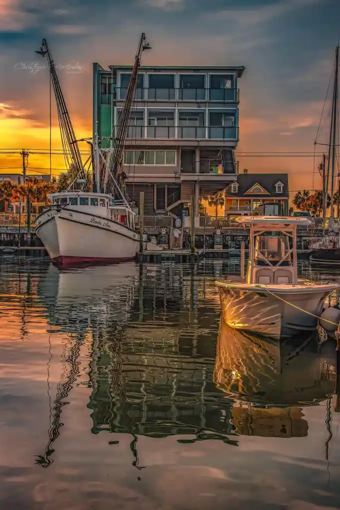 A serene harbor scene at sunset with a large white fishing boat named 'Linda Ann' docked next to a modern multi-story…