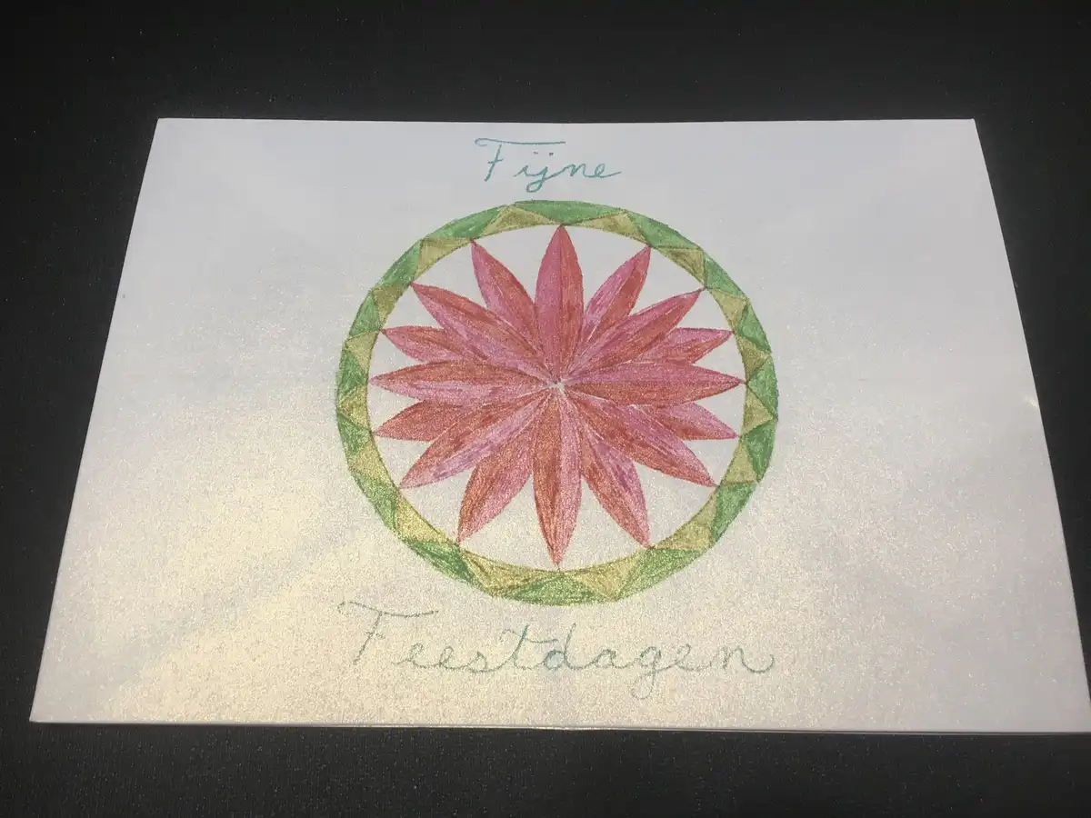 A hand-drawn greeting card on textured white paper, featuring a colorful mandala-style flower with pink petals and a green…