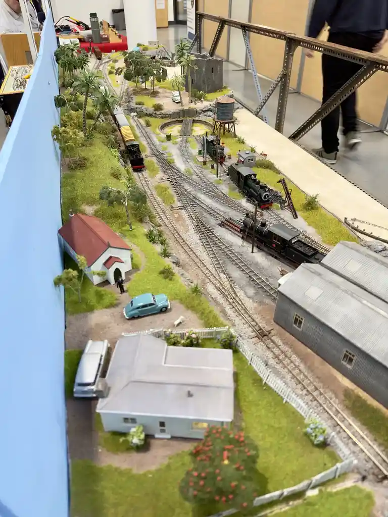 An overhead view of a highly detailed model train layout featuring miniature trains, tracks, buildings, trees, and cars on a…