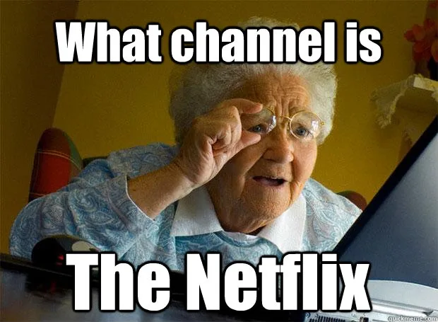 An elderly woman with white hair and glasses, wearing a blue patterned shirt, sits in front of a laptop and adjusts her…