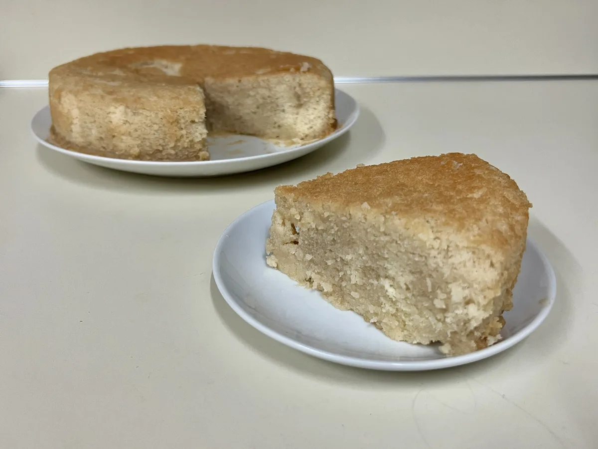 A plain, unadorned cake sits on a white plate in the background with a single slice removed, while the same slice is…