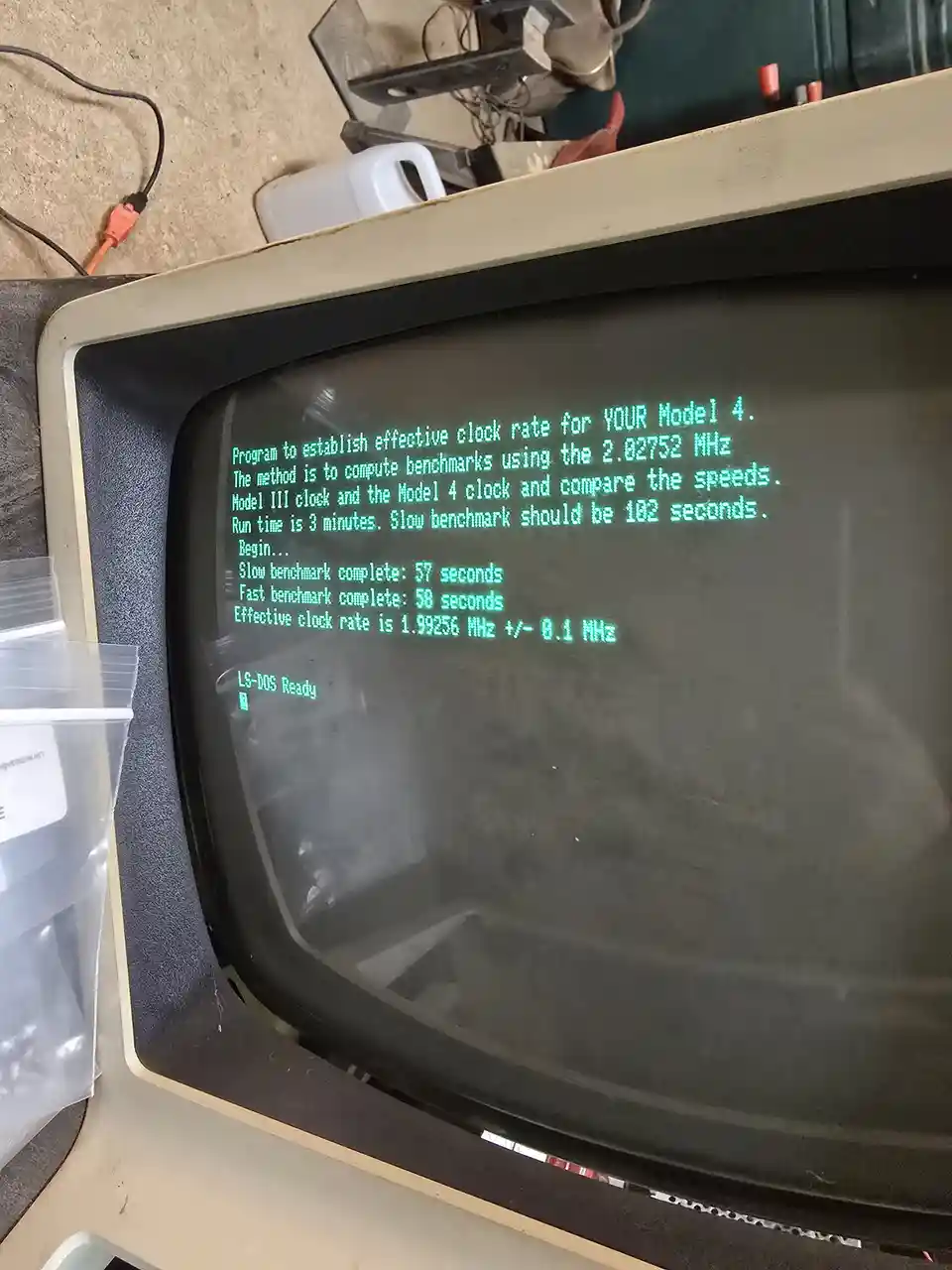 An old CRT monitor displays green text from a vintage computer benchmark program running on an Apple IIgs, showing results…