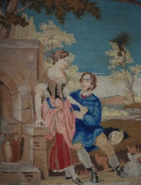 A vintage tapestry depicts a man in a blue outfit and red bow tie kneeling before a woman in a pink and red dress, holding…
