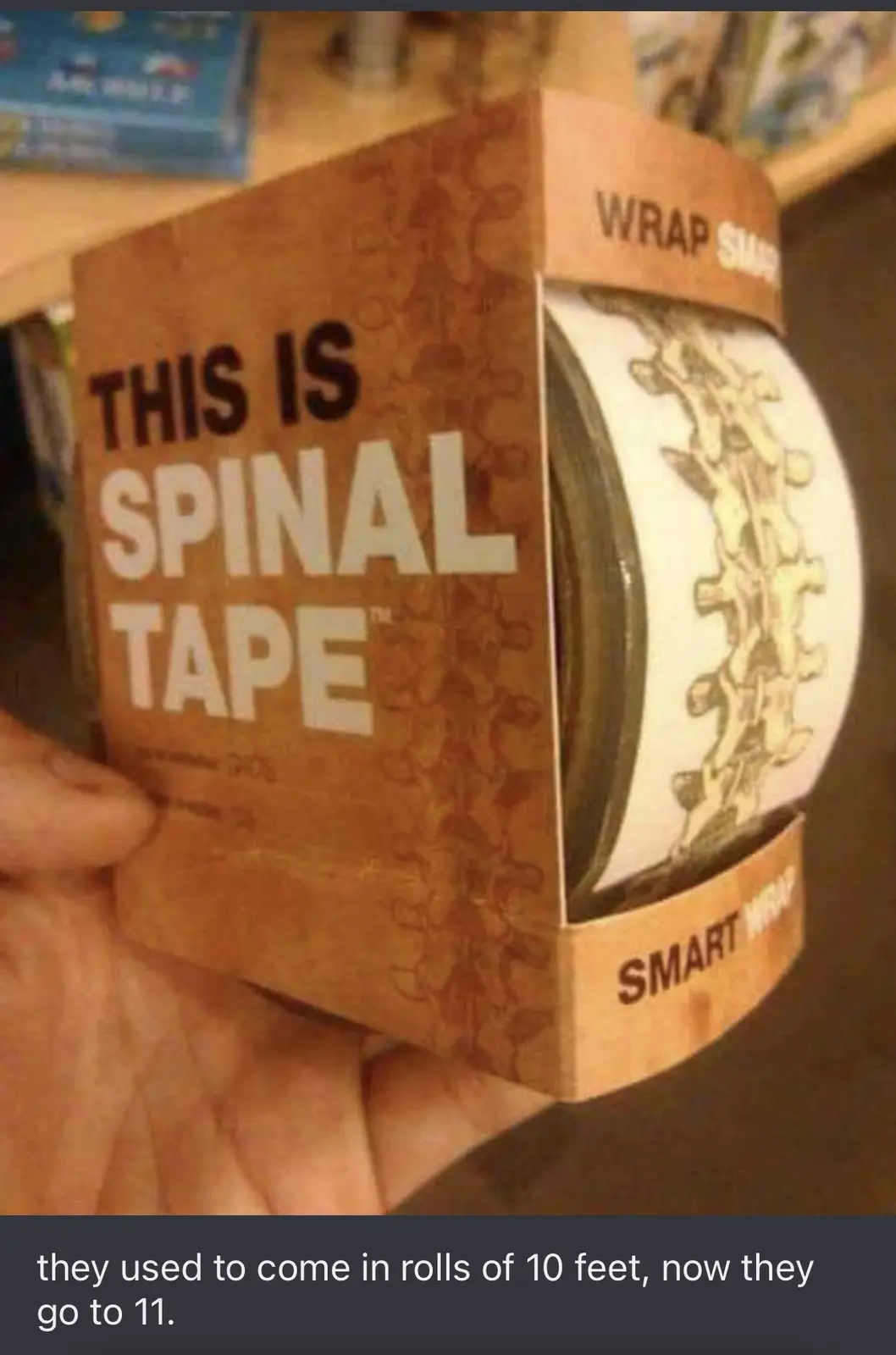 A hand holds a cardboard box labeled 'THIS IS SPINAL TAPE™' with a roll of tape inside featuring a spinal column design. The…
