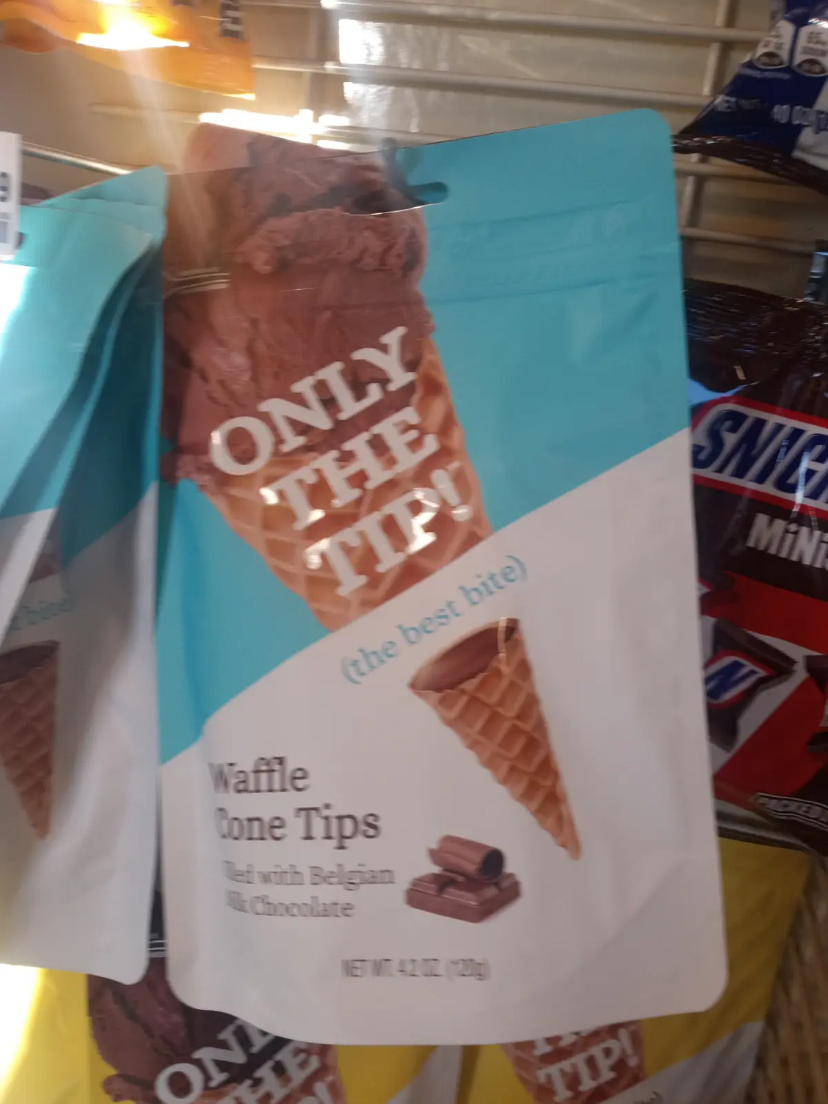 A close-up of a retail package for 'Waffle Cone Tips' filled with Belgian milk chocolate, prominently displaying the slogan…