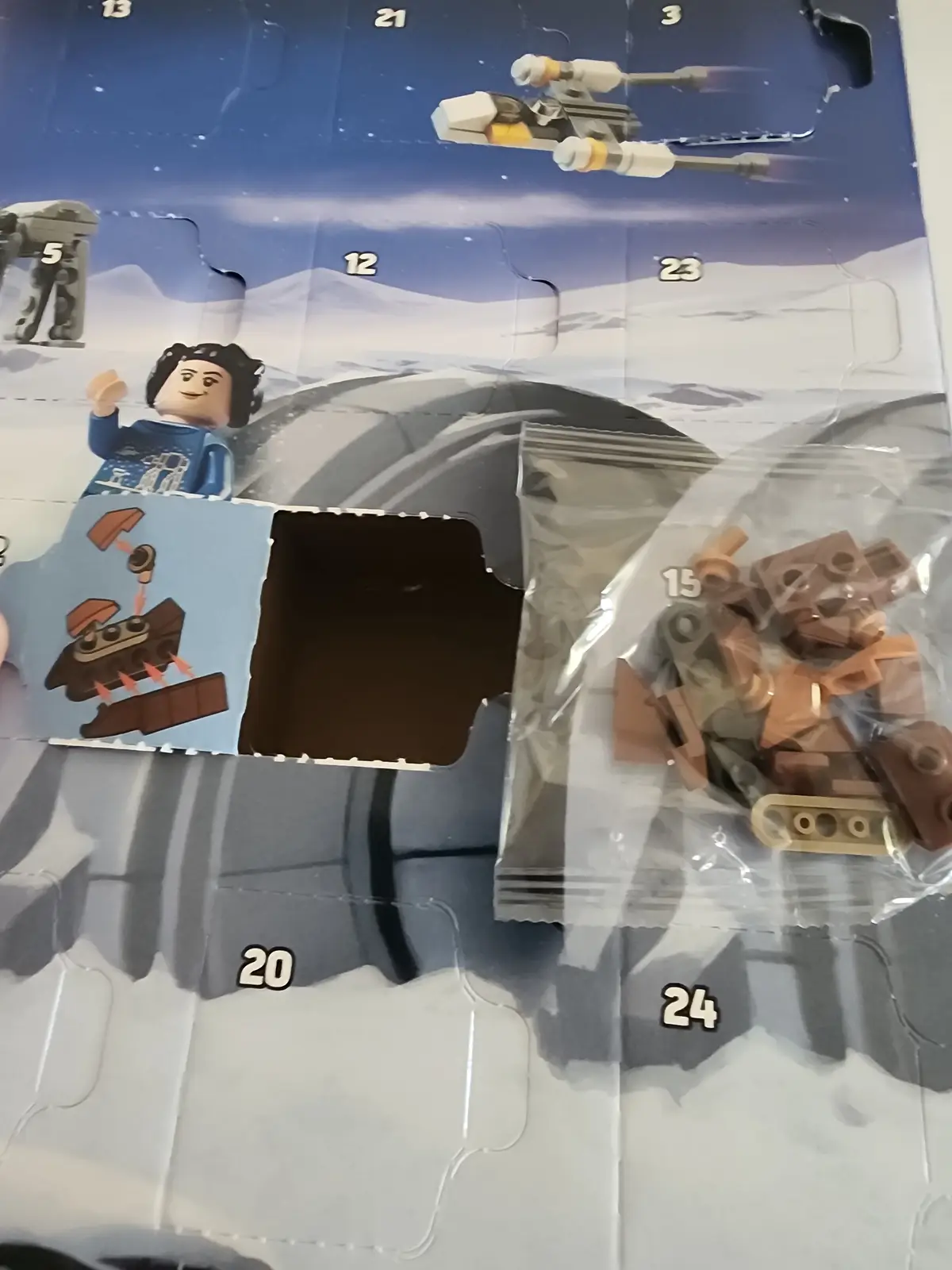 A close-up photo shows an opened LEGO Star Wars Advent Calendar with compartment 15 ripped open, revealing a clear plastic…