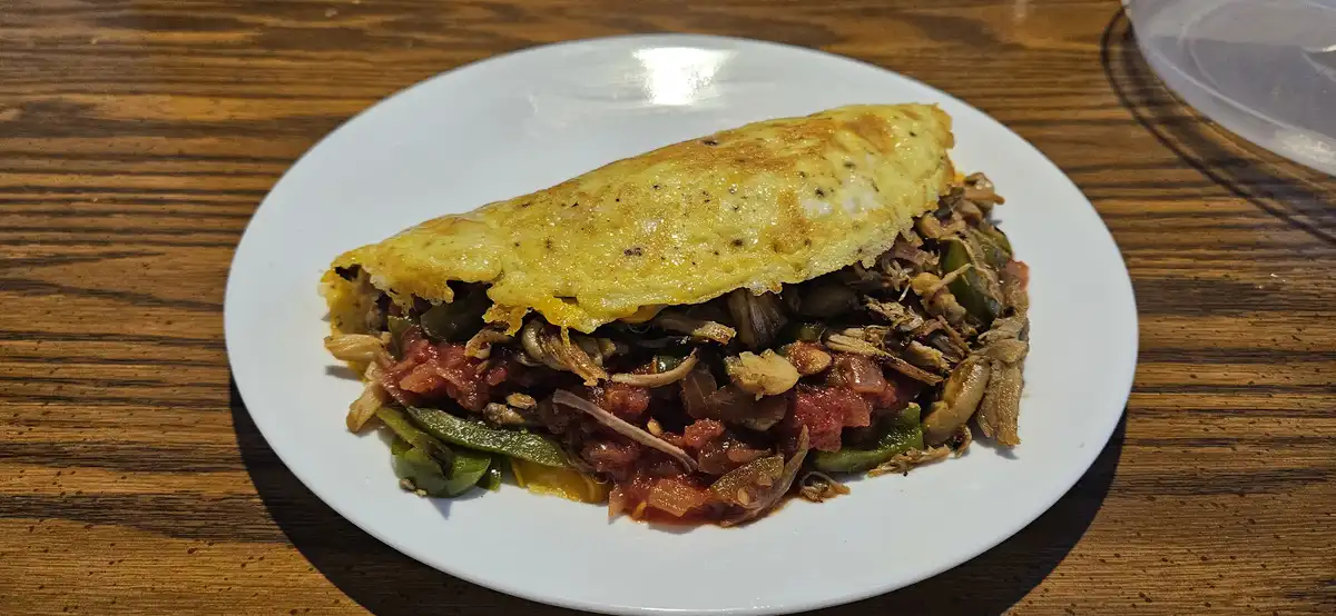 A close-up photo shows a folded, golden-brown omelette on a white plate, revealing a filling of shredded meat, green…