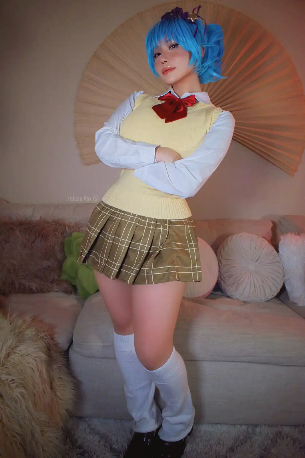 A person with bright blue hair styled in pigtails and wearing a school uniform consisting of a white shirt, yellow sweater…