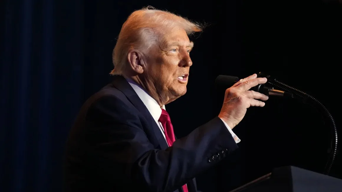 a man in a dark suit and red tie speaks into a microphone while gesturing with his hand. The overlaid text reads: 'i'm not a…