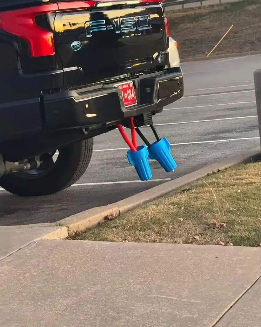 The rear of a black Ford F-150 pickup truck is shown parked in a lot, with its hitch attached to two blue plastic cups…