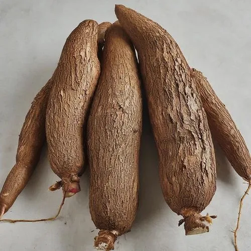 A pile of rough-skinned, brown yams with tapered ends and visible roots lie on a light gray surface. Overlaid text reads…