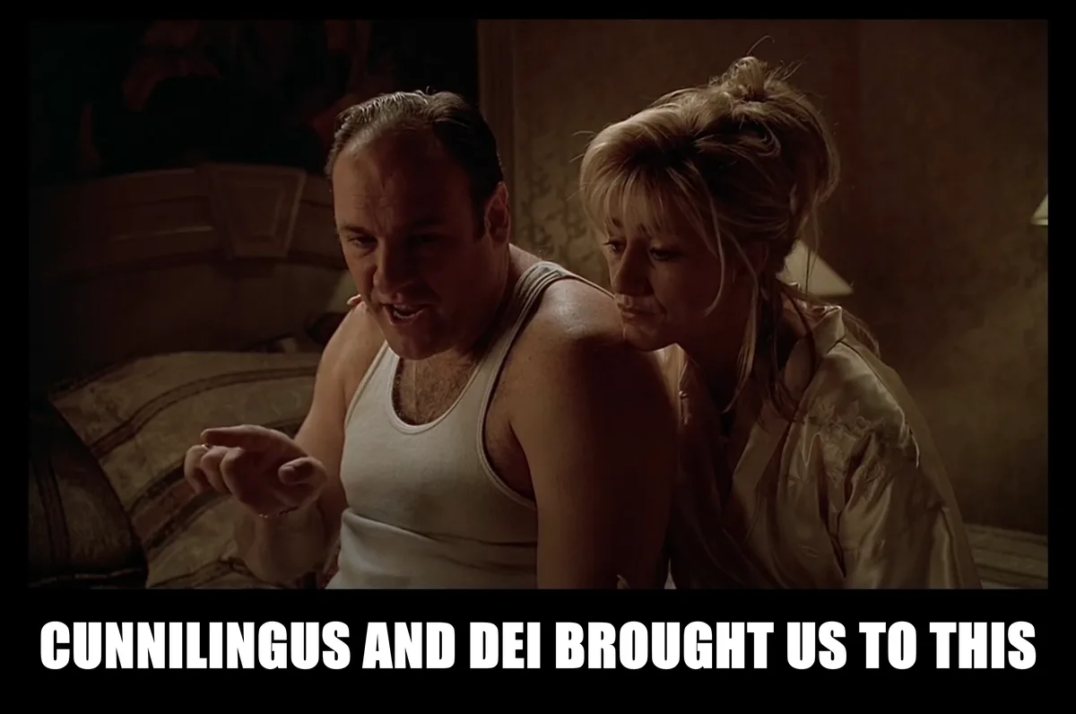 A man in a white tank top and a woman in a satin robe sit on a bed in a dimly lit room, looking at something off-screen with…