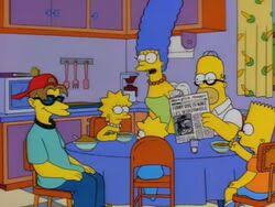 The Simpson family is seated at their kitchen table. Marge Simpson, with her iconic blue beehive hairdo, is standing and…