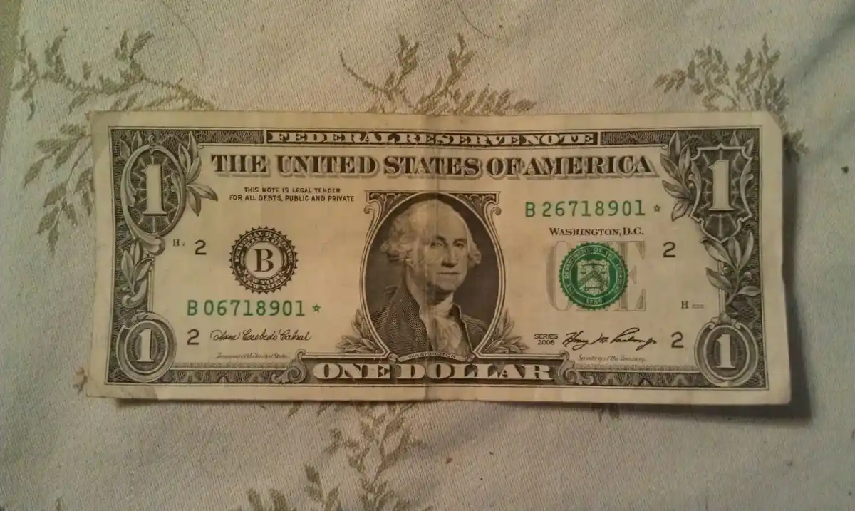 A slightly worn one-dollar U.S. Federal Reserve Note featuring George Washington's portrait is laid flat on a patterned…