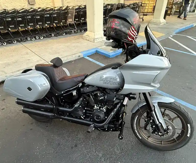 A silver and black Harley-Davidson motorcycle is parked in a store parking lot, with a black helmet resting on the…