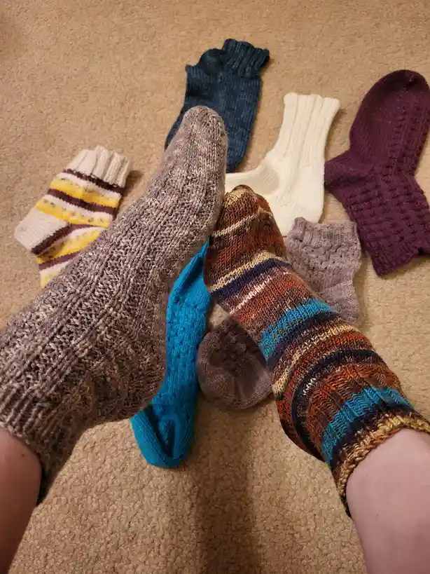 A person's feet, one wearing a plain brown knit sock and the other a colorful striped sock, are shown on a beige carpet…