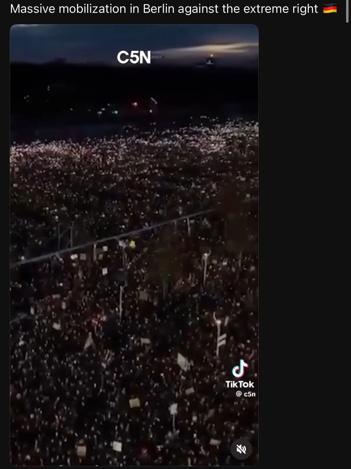 An aerial night view shows a massive crowd of people holding up phones or signs, creating a sea of lights. The image has…