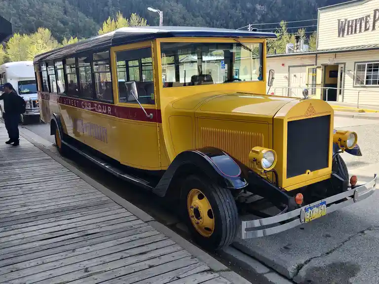 A vintage yellow streetcar labeled 'ALASKA STREET CAR TOUR' and 'MAIN POINTS OF INTEREST' is parked beside a wooden…