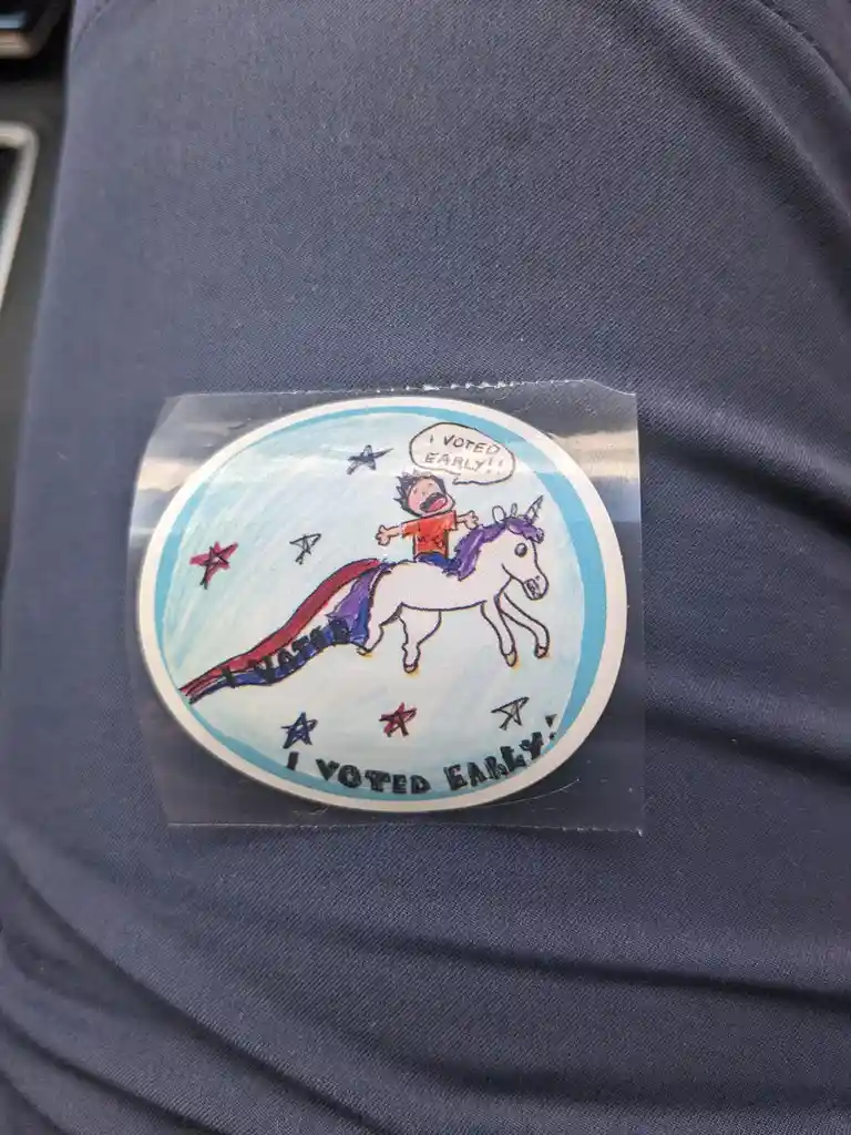 A circular sticker on a dark blue fabric shows a cartoon boy riding a white unicorn with a rainbow mane and tail through a…