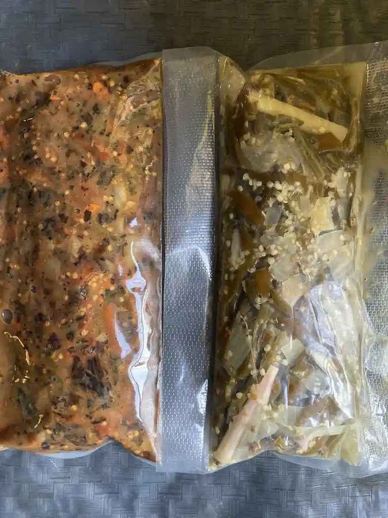 Two vacuum-sealed plastic bags sit side-by-side on a woven gray surface. The left bag contains a dark, chunky, reddish-brown…