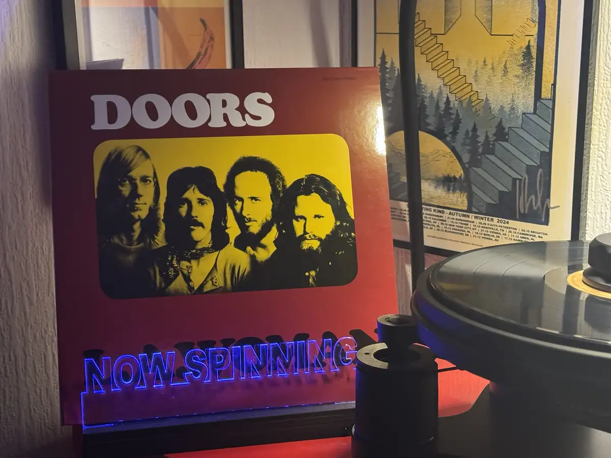A red Doors album cover featuring the band's four members in a yellow-bordered photo stands next to a record player with a…