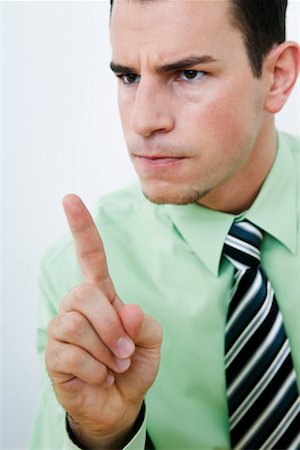 A man in a light green shirt and striped tie points his index finger directly at the viewer with a stern, disapproving…