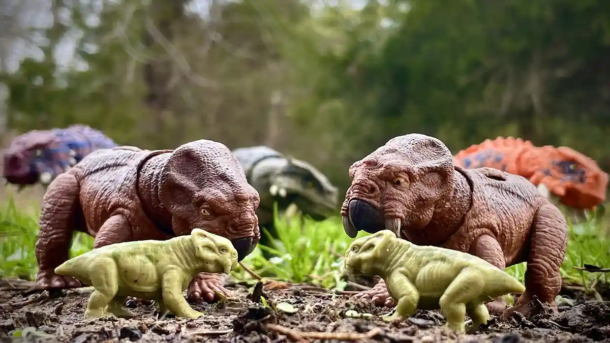 Two large, brown, toy dinosaurs with tusks and angry expressions face each other, each with a smaller, green, toy dinosaur…