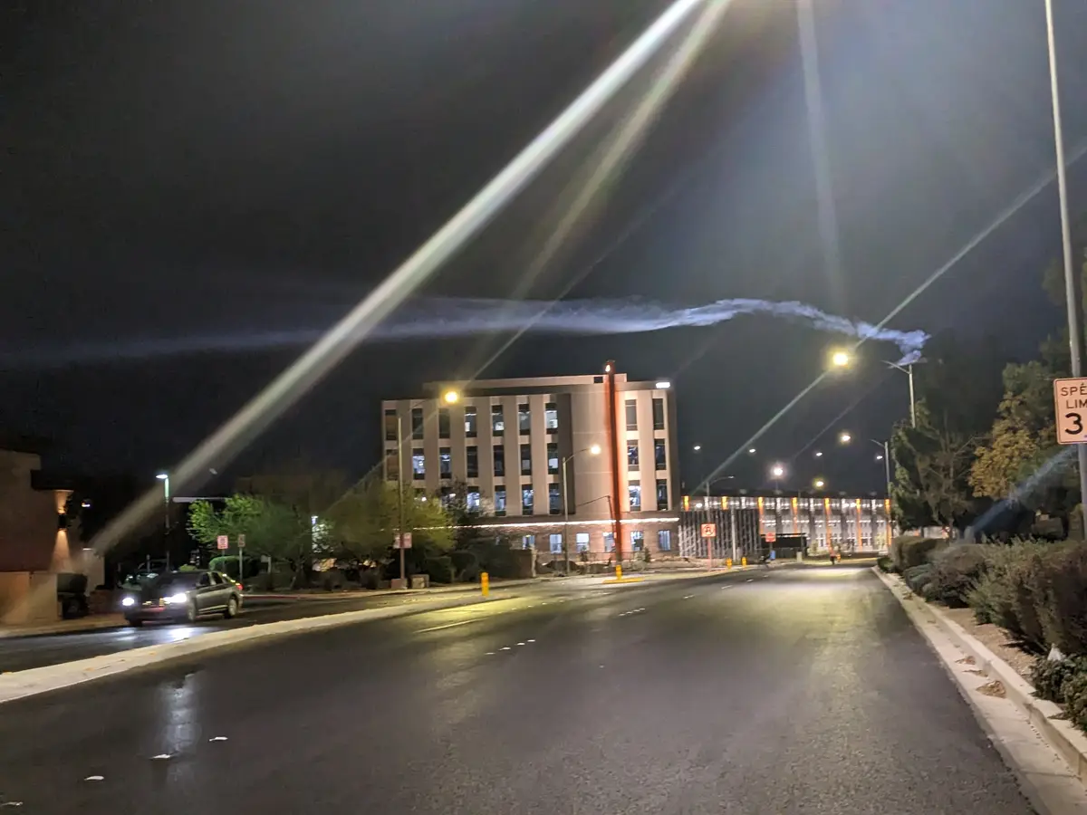 A nighttime street scene with a multi-story building, streetlights, and a car on the road. A speed limit sign reads 'SPEED…