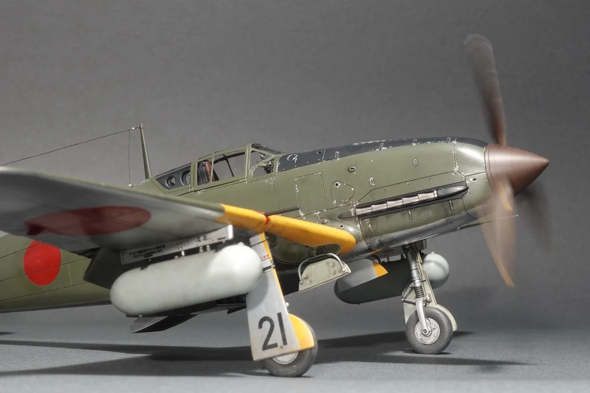 A detailed scale model of a Japanese military aircraft, likely a Nakadžima NK-14, is shown on a grey surface with its…