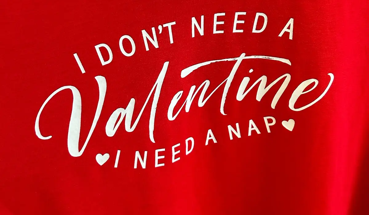 A close-up of a red t-shirt with white text that reads 'I DON'T NEED A Valentine I NEED A NAP', with 'Valentine' in a large…