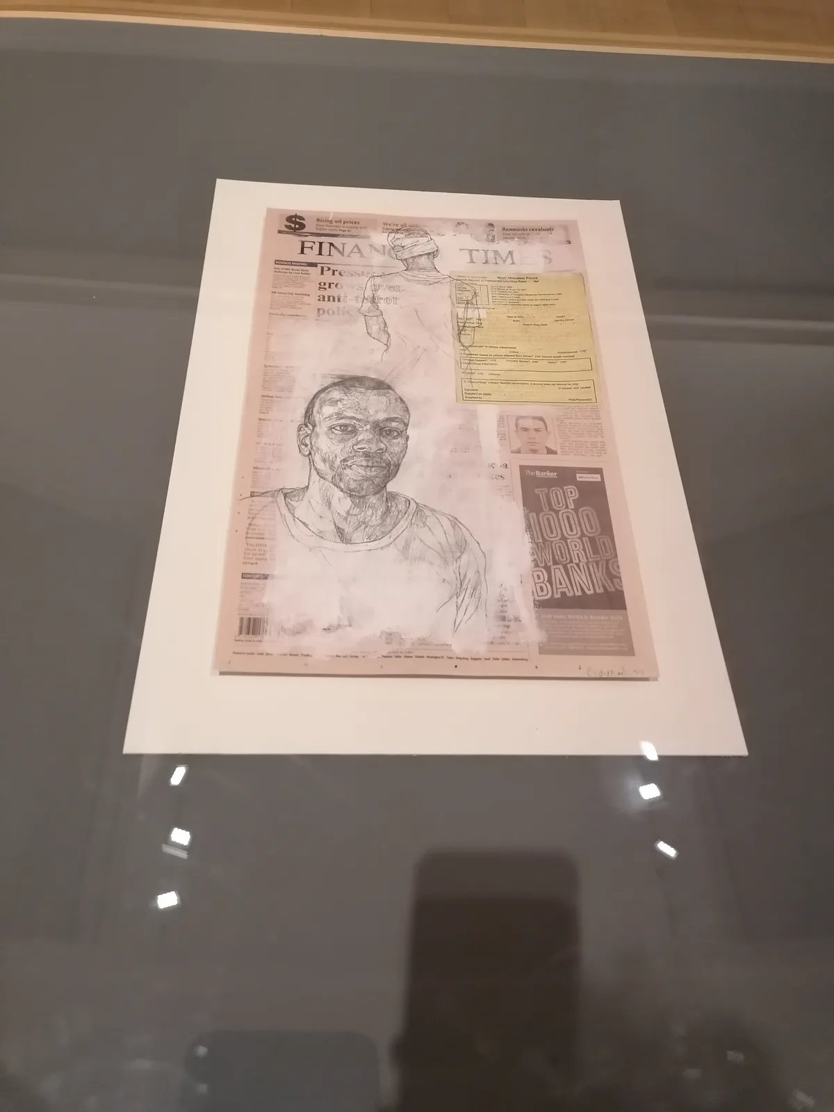 A framed artwork displayed behind glass, featuring a newspaper collage with 'FINANCIAL TIMES' visible, overlaid with a…