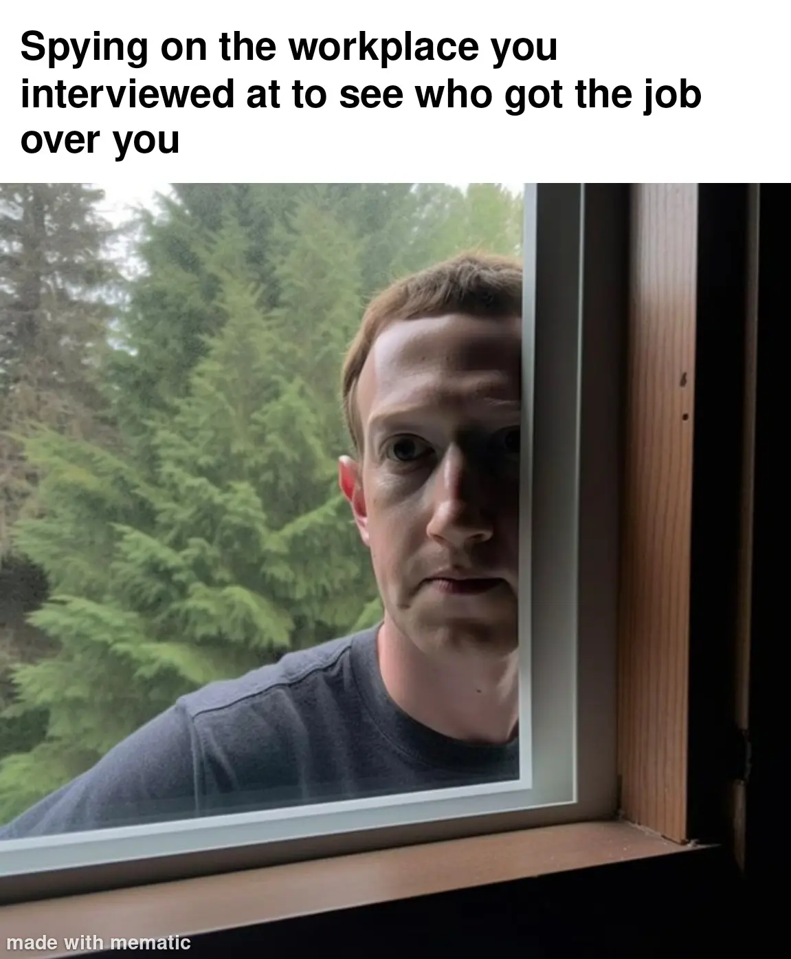 A man with short brown hair and a gray t-shirt peers through a window frame, looking intently at the viewer with a serious…
