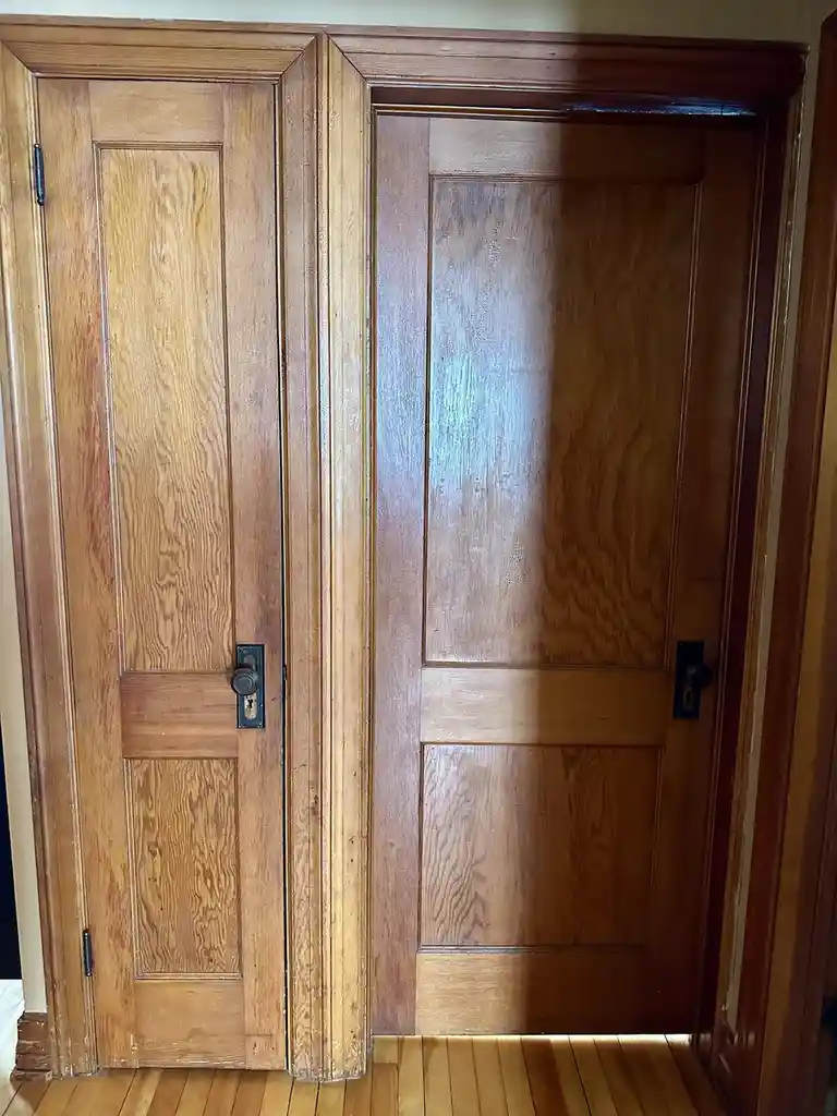 A side-by-side photo shows two wooden doors in a hallway; the left door is lighter in color and appears worn, while the…