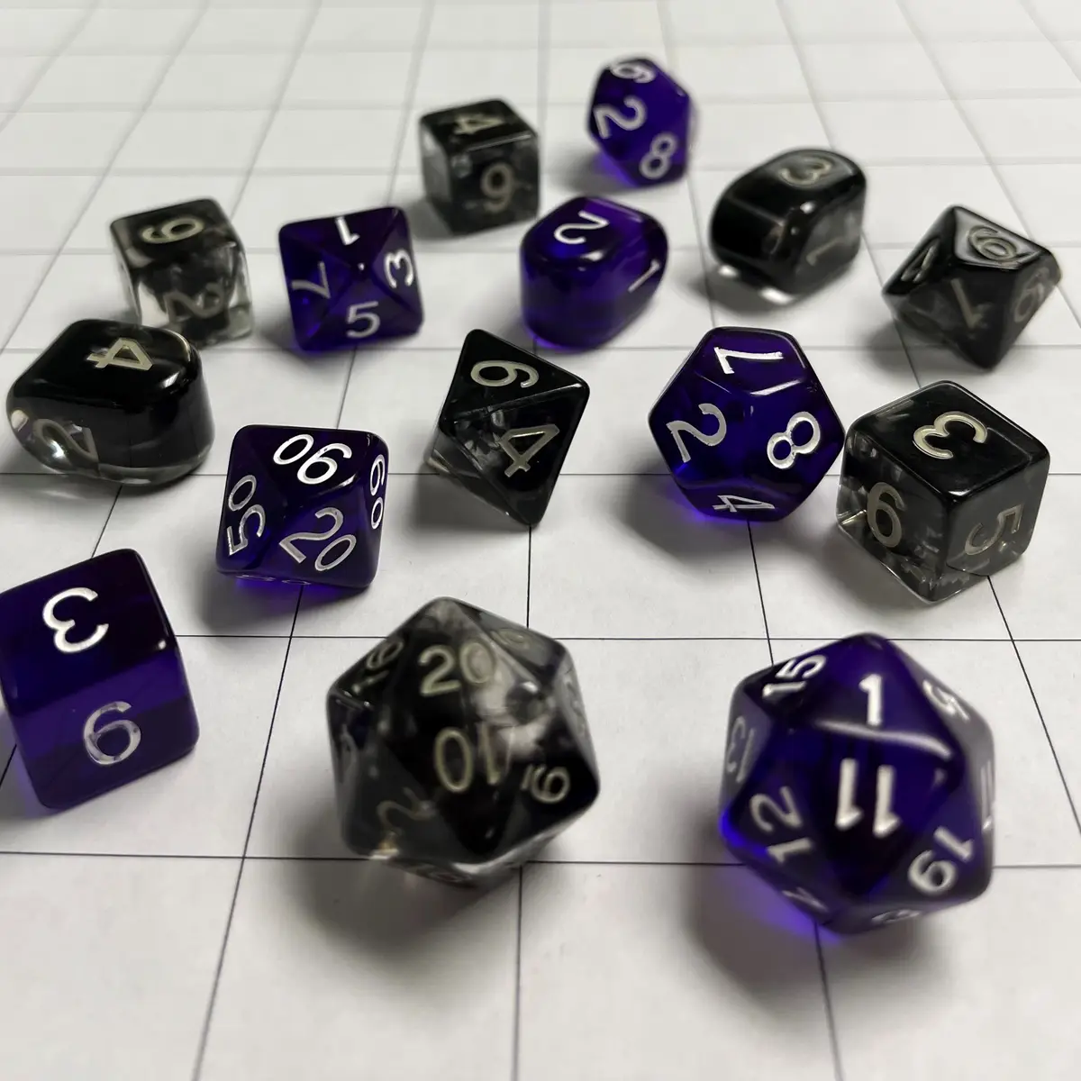 A collection of various polyhedral dice, including black, translucent black, and purple ones, are scattered on a white…