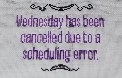 A close-up of purple cross-stitch text on light gray fabric reads 'Wednesday has been cancelled due to a scheduling error.'…