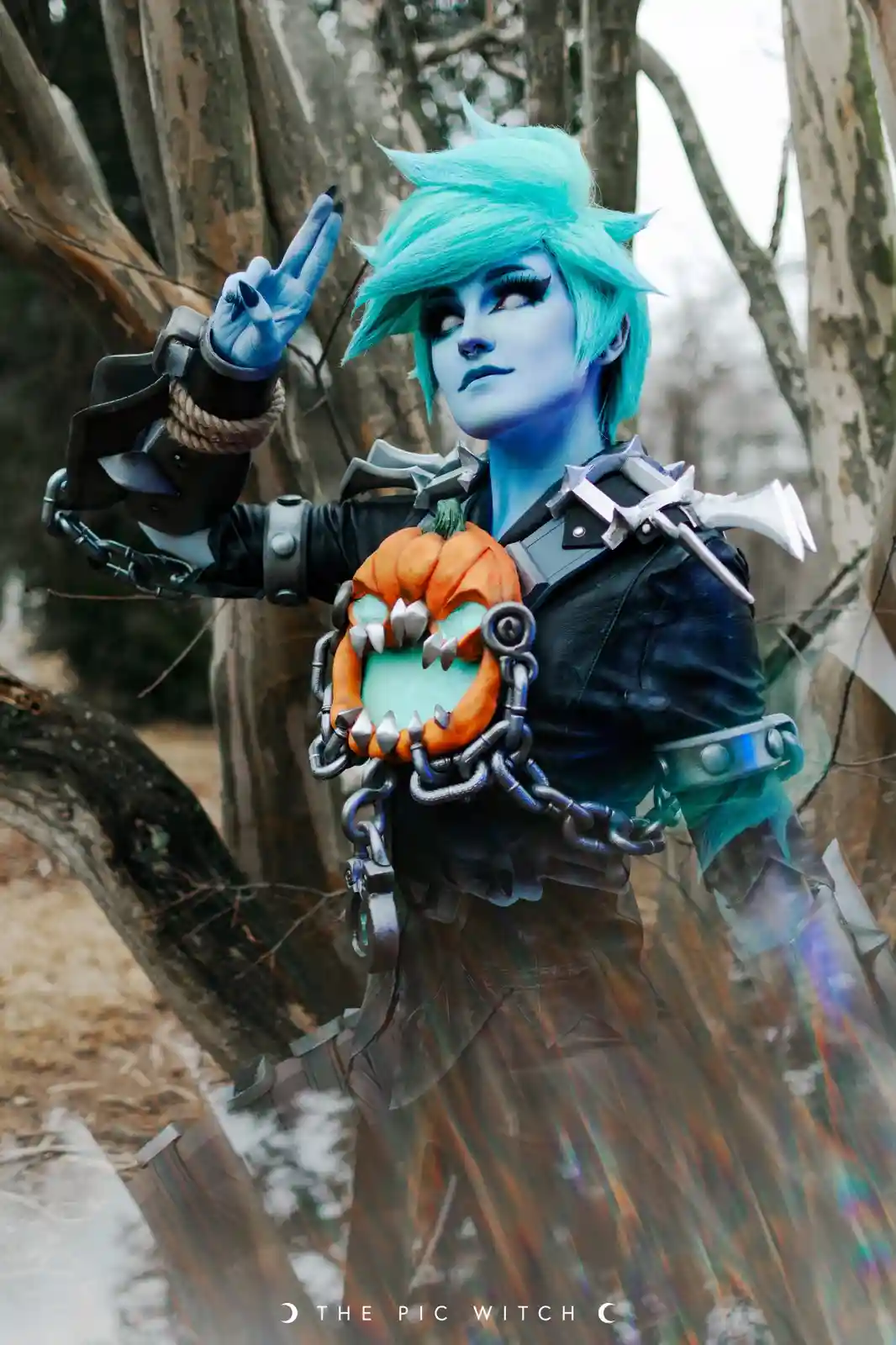 A person in a detailed cosplay of a blue-skinned, spiky-haired character with a pumpkin-headed weapon strapped to their…