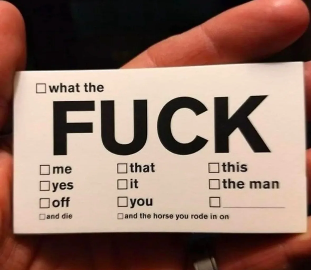 A hand holds a white card with bold black text reading 'what the FUCK' at the top. Below, checkboxes list options like 'me'…