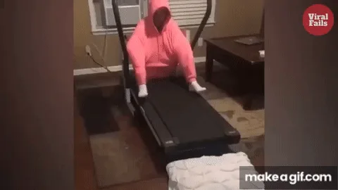 A person in a pink hooded outfit is on a treadmill, then suddenly falls backward off the machine in a comedic fashion. The…