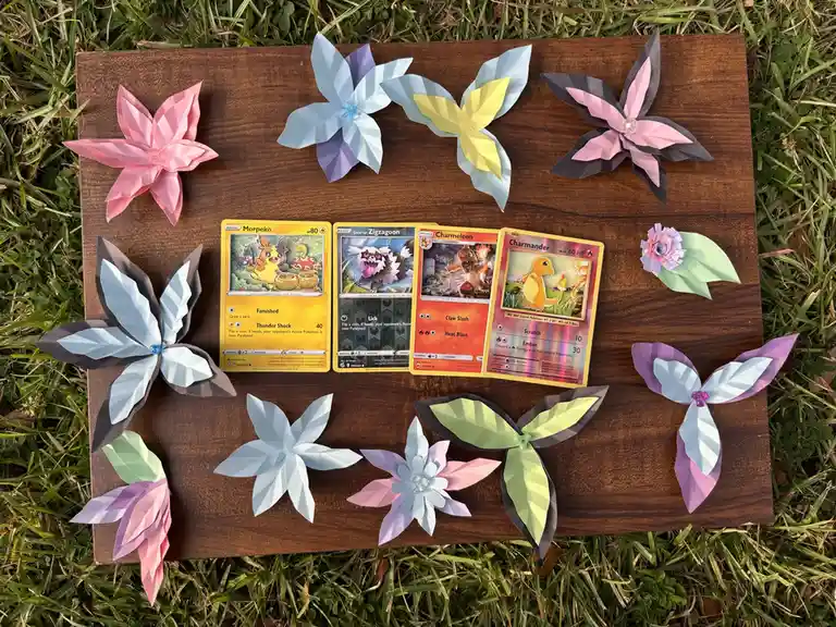 Four pokemon trading cards — Morpeko, Galarian Zigzagoon, Charmeleon, and Charmander — are laid out on a wooden board…