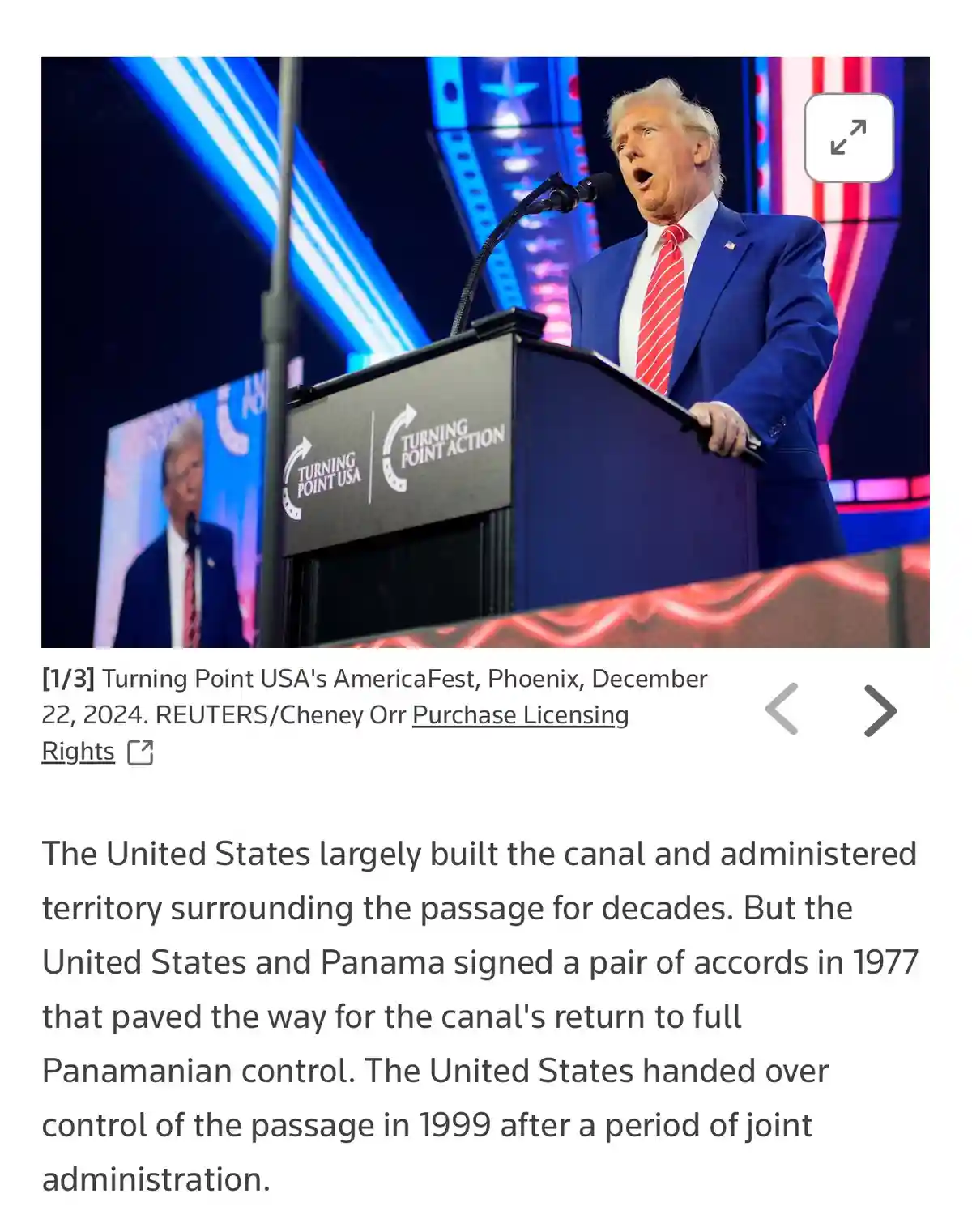 A man in a blue suit and red tie stands at a podium with 'Turning Point USA' and 'Turning Point Action' logos, speaking into…