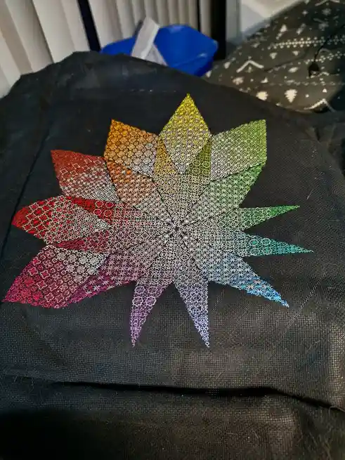 A black fabric item, likely a tote bag or pillow, features a large, intricate embroidered starburst design with…