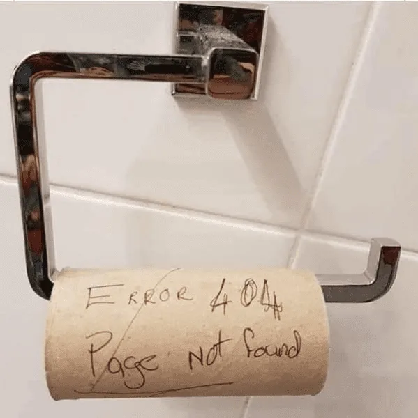A toilet paper roll on a chrome holder in a tiled bathroom has 'Error 404 Page not found' handwritten on it in black marker…