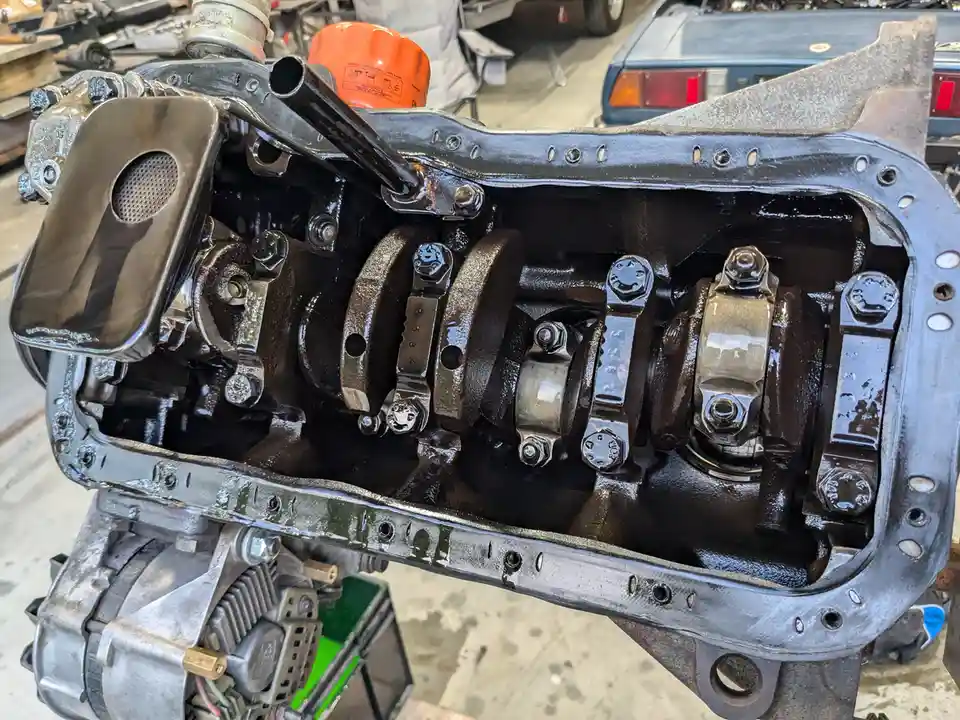A close-up photo of a freshly rebuilt car engine block with its internal components exposed, showing shiny new bolts and…