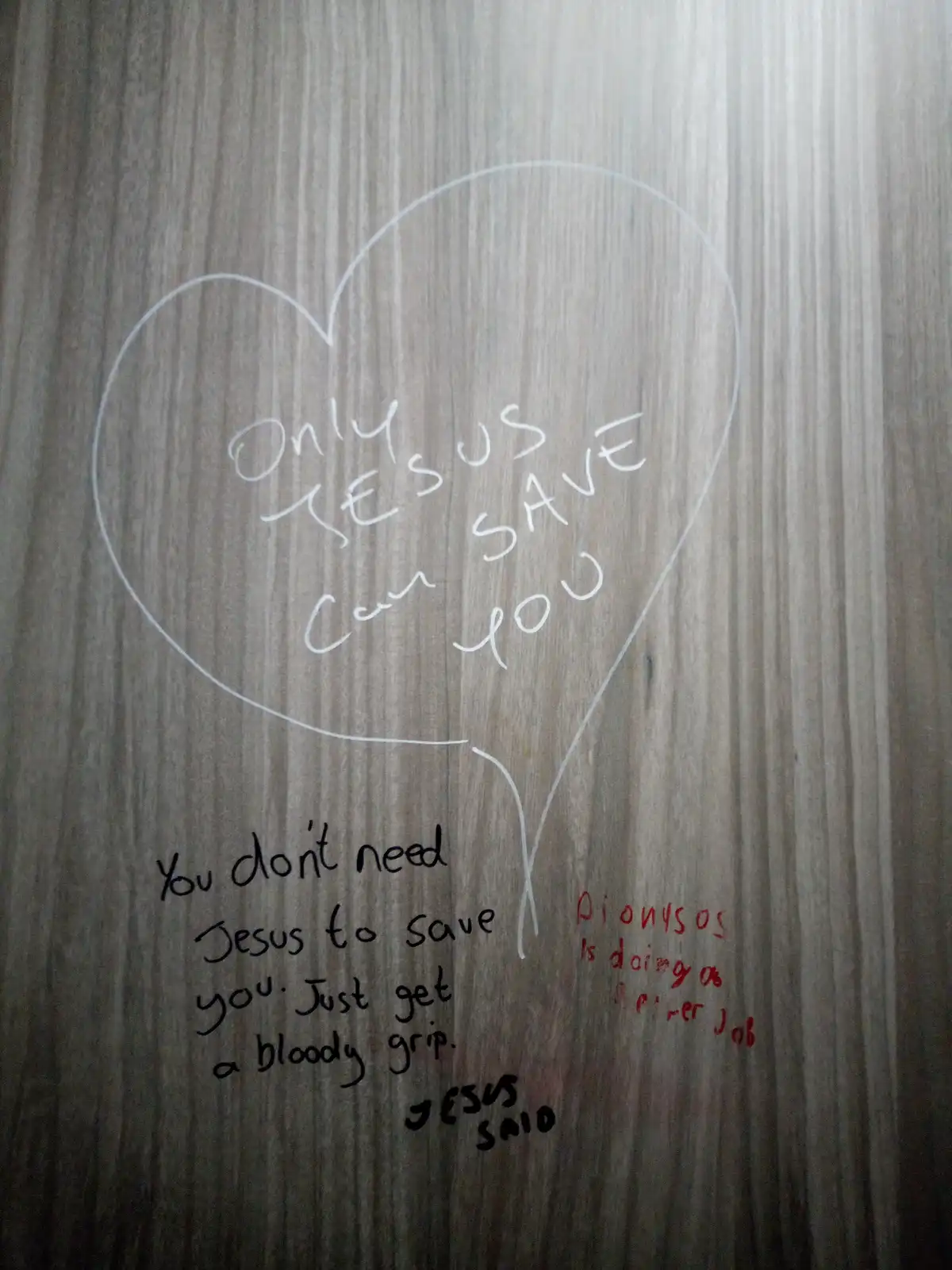 A close-up of a wooden surface with white chalk-like writing inside a heart shape reading 'Only Jesus Can Save You'. Below…