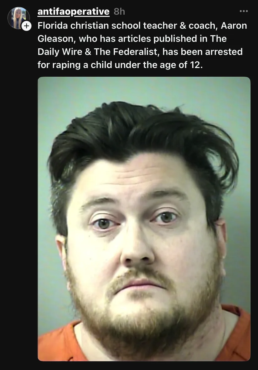 A mugshot of a man with dark hair and a beard wearing an orange shirt against a plain background. Overlaid text states that…