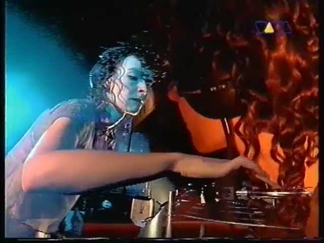 A person with wet, curly hair is shown in a dimly lit setting, possibly a stage or studio, reaching toward a control panel…