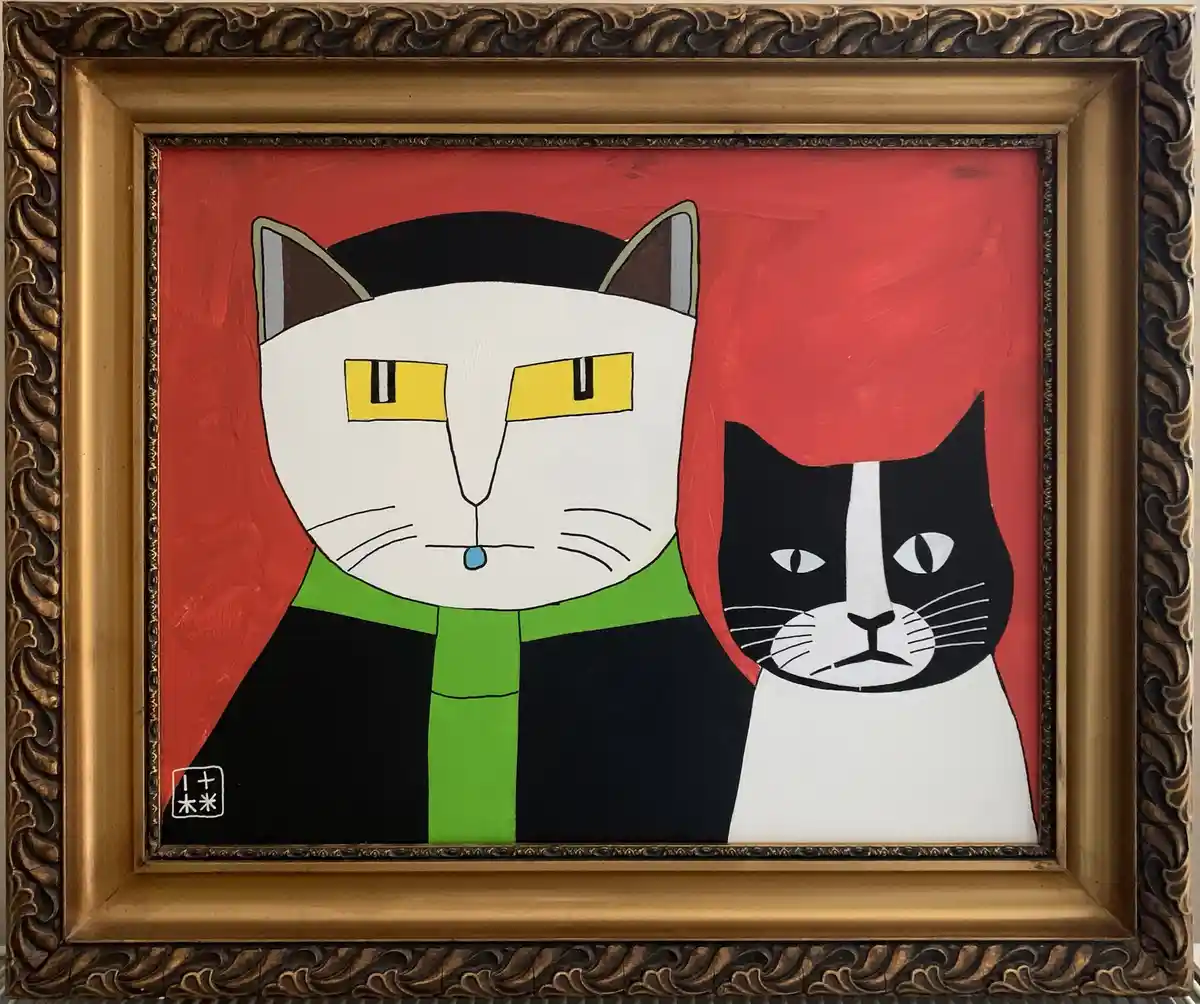 A framed painting depicts two stylized cats against a red background; the larger white cat on the left wears a green scarf…