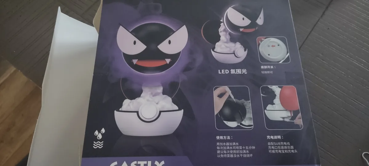 The image shows a product box for a mist machine shaped like the Pokémon character Gastly. The box features a large…